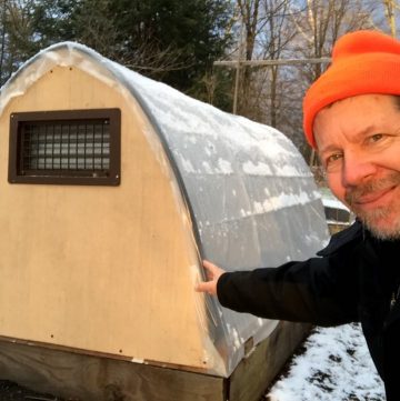 A man next to a greenhouse in the snow